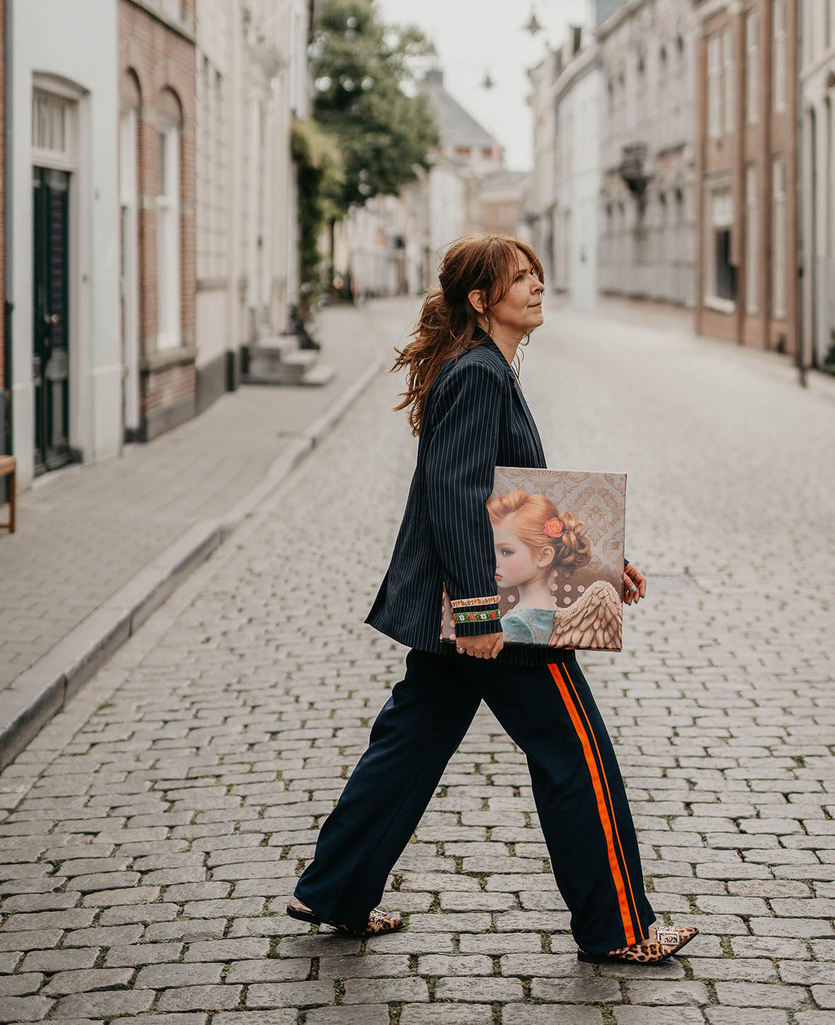 Vrouw loopt met art print onder haar arm door rustige straat, zelfverzekerde houding, sfeer van creatieve vrijheid